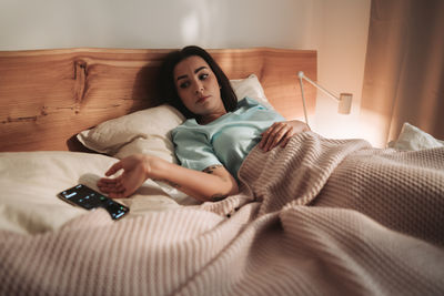 Young woman using mobile phone while lying on bed at home