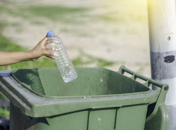 Cropped image of hand holding bottle over garbage bin