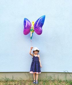 Full length of girl holding balloon while standing against wall