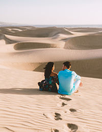 Rear view of woman sitting on sand at beach