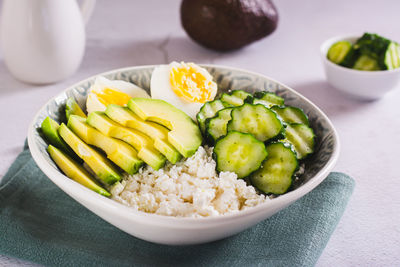 Bowl with cottage cheese, cucumber and avocado slices and boiled egg on the table