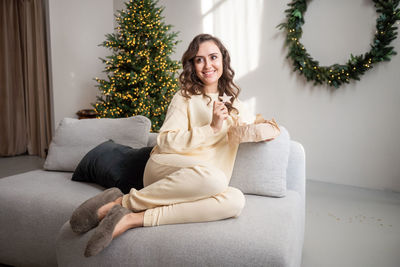 A cute girl with glasses is sitting at home on the couch and holding a ginger cookie in the shape 