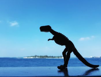 Toy dinosaur silhouette on blue sky and sea