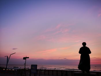 Rear view of silhouette man standing at beach against sky during sunset