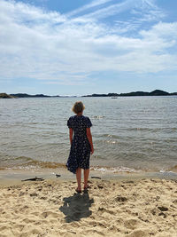 Rear view of woman standing at beach against sky