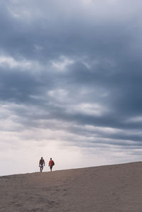 Rear view of people walking at desert against cloudy sky