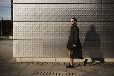 Businessman wearing jacket carrying briefcase while walking against silver colored wall