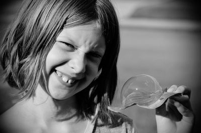 Close-up portrait of smiling girl holding bubble on leaf during sunny day