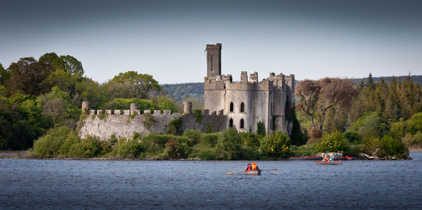 Castle at riverbank against sky