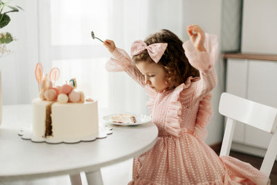 Cute little girl eats a birthday cake with a spoon on her birthday