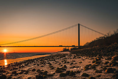 View of suspension bridge at beach during sunset