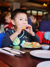 Portrait of boy eating food on table at restaurant