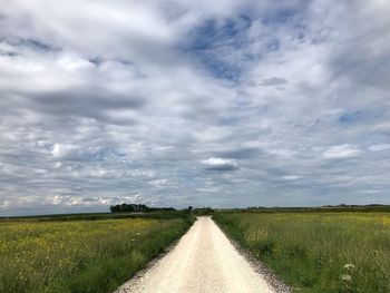 Empty road amidst field against sky