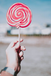Cropped hand of woman holding lollipop against sky