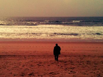 Rear view of silhouette man standing on beach at sunset