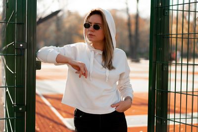 Woman wearing sunglasses while standing against metal gate
