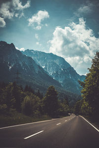 Country road by mountains against sky