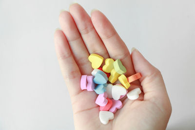 Cropped hand of person holding multi colored candies against white background