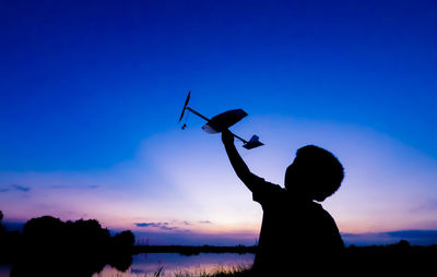 Silhouette of boy playing with toy airplane against sky