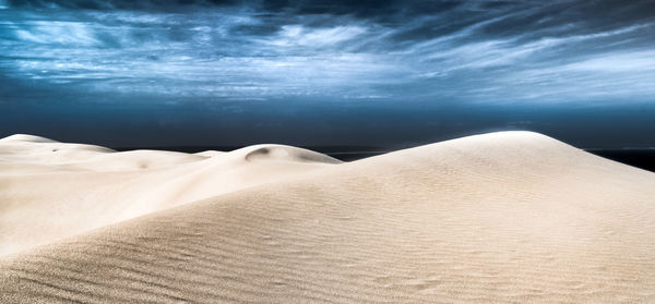 Scenic view of sand dunes at desert against cloudy sky