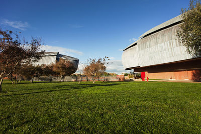 Auditorium in front of grassy field against sky on sunny day