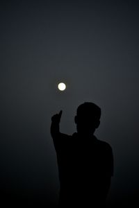 Silhouette man pointing at moon against sky at night