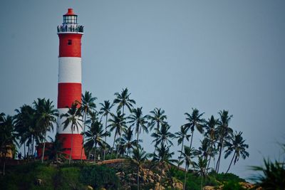 Lighthouse by coconut palm trees on field against sky