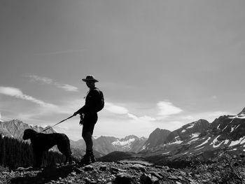 Man standing on mountain against sky with dog