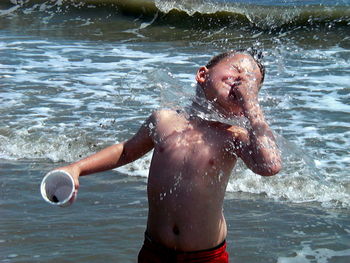 Shirtless boy playing with water in sea