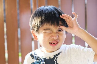 Portrait of playful boy making face against fence