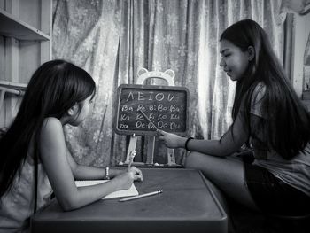 Side view of teenage girl teaching sister alphabets at home