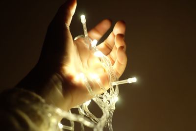 Close-up of hand holding lit candle against black background