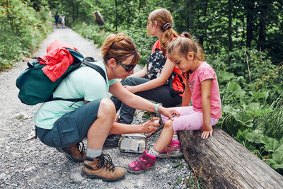 Mother dressing the wound on her little daughter's knee with medicine in spray. accident during trip