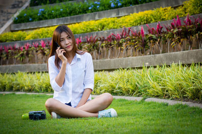 Young woman using phone while sitting on grass