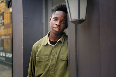Portrait of young black skin man standing against wooden door.