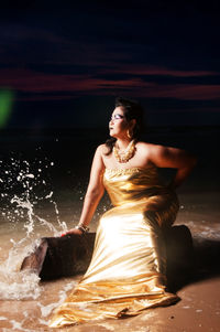 Woman wearing evening gown while sitting on seashore at night