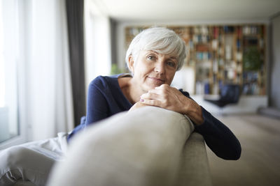 Contemplating senior woman relaxing while sitting on sofa