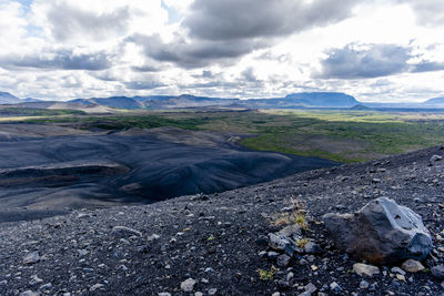 Lava rocks on stretch of sand with cloudy blue sky at lake mivatn in iceland