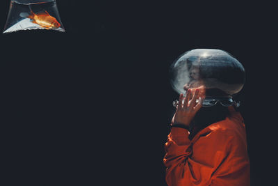 Side view of man wearing container on face while looking at fish against black background