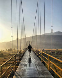 Rear view of man walking on footbridge against sky