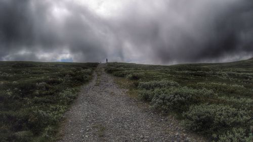 Road passing through field against cloudy sky