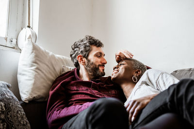 Young bearded man in casual shirt lying on comfortable couch in embrace with african american woman in cozy living room with closed eyes