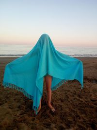 Girl with blue scarf standing at beach against clear sky during sunset