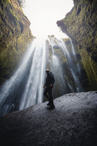 Man standing on rock against waterfall