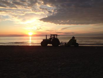 Silhouette tractor on beach against sky during sunset