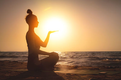Silhouette woman standing at beach against sky during sunset