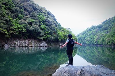 Rear view of man standing on rock by river against sky