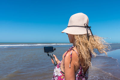 Woman using a mobile phone with a tripod while the wind moves her hair on the beach