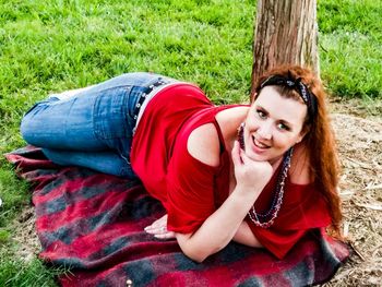 Portrait of beautiful woman lying on field against tree trunk