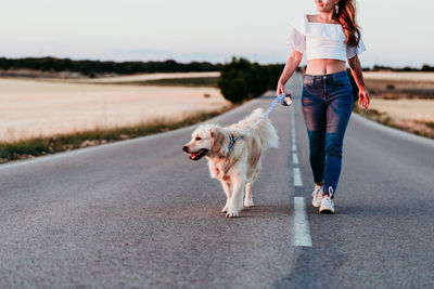 Woman walking with dog on road amidst field